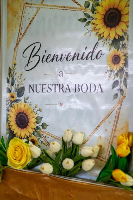 Cartel de bienvenida a nuestra boda con girasoles y un arreglo de flores amarillas y blancas.
