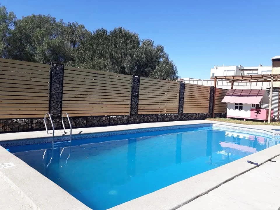 Piscina de Manantial al aire libre, junto a una cerca de madera y bajo un cielo despejado.